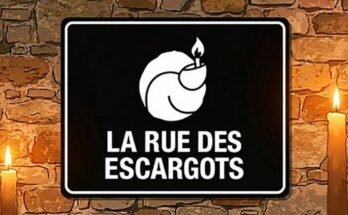 Panneau noir de la Rue des Escargots, avec un escargot et une flamme blancs entre deux bougies.