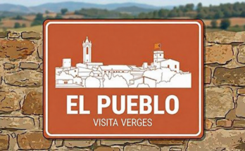 Silueta de Verges en un cartel sobre un muro de piedra, con el texto «El pueblo · Visita Verges».