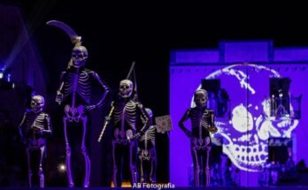 Danseurs de la Danse de la Mort en costumes de squelette sur une place éclairée en violet.