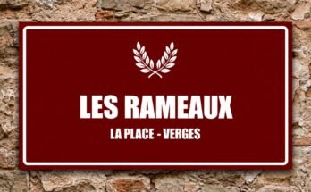 Deux branches blanches croisées sur un panneau rouge «Les Rameaux · La Place, Verges».