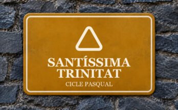 Rètol ocre sobre un mur de pissarra amb un pictograma i el text «SANTÍSSIMA TRINITAT».