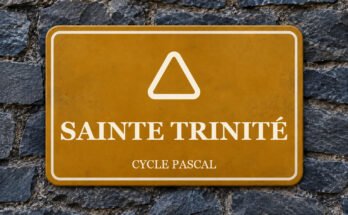 Panneau ocre sur un mur d’ardoise, avec un pictogramme et le texte «SAINTE TRINITÉ».