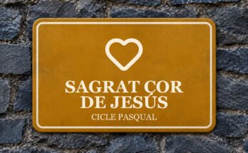 Rètol ocre sobre un mur de pissarra amb un pictograma i el text «SAGRAT COR DE JESÚS».