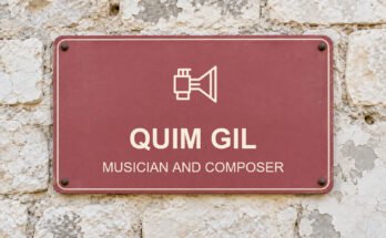 Dusty-rose sign on a limestone wall reading “QUIM GIL”, with a pictogram.