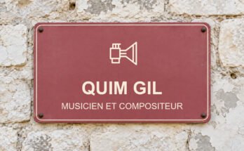 Panneau rose sur un mur en pierre calcaire portant le texte «QUIM GIL» et un pictogramme.