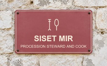 Dusty-rose sign on a limestone wall reading “SISET MIR”, with a pictogram.