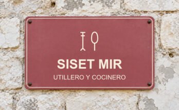 Rótulo rosa sobre un muro de piedra caliza con el texto «SISET MIR» y un pictograma.