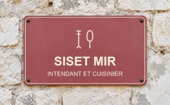 Panneau rose sur un mur en pierre calcaire portant le texte «SISET MIR» et un pictogramme.