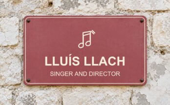 Dusty-rose sign on a limestone wall reading “LLUÍS LLACH”, with a pictogram.