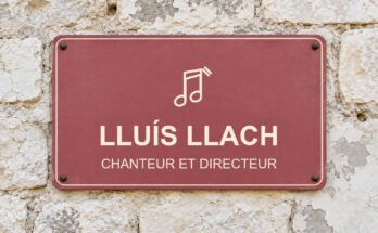 Panneau rose sur un mur en pierre calcaire portant le texte «LLUÍS LLACH» et un pictogramme.