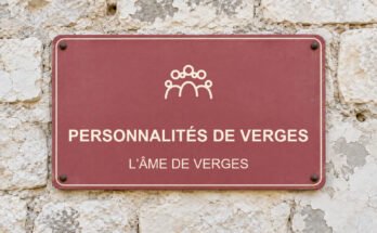 Panneau rose sur un mur en pierre calcaire portant le texte «PERSONNALITÉS DE VERGES» et un pictogramme.