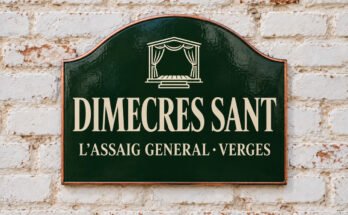 Rètol verd arquejat amb «DIMECRES SANT» i un escenari amb cortines, sobre un mur de maó emblanquinat.