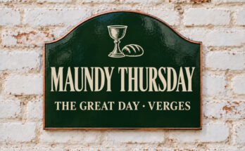 Arched green sign reading “MAUNDY THURSDAY”, with bread and a chalice, on a whitewashed brick wall.