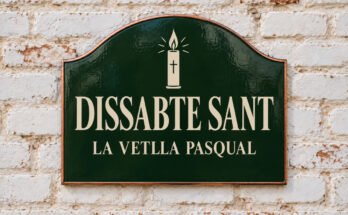 Rètol verd arquejat amb «DISSABTE SANT» i un ciri pasqual, sobre un mur de maó emblanquinat.