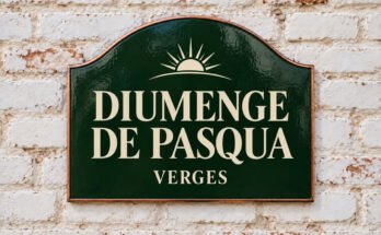 Rètol verd arquejat amb «DIUMENGE DE PASQUA» i una sortida de sol, sobre un mur de maó emblanquinat.