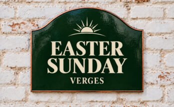 Arched green sign reading “EASTER SUNDAY”, with a sunrise, on a whitewashed brick wall.