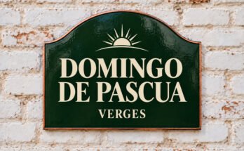 Rótulo verde arqueado con «DOMINGO DE PASCUA» y un amanecer, sobre un muro de ladrillo encalado.