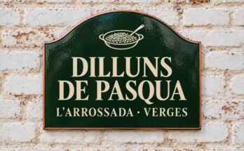 Rètol verd arquejat amb «DILLUNS DE PASQUA» i un plat d’arròs i una cullera, sobre un mur de maó emblanquinat.